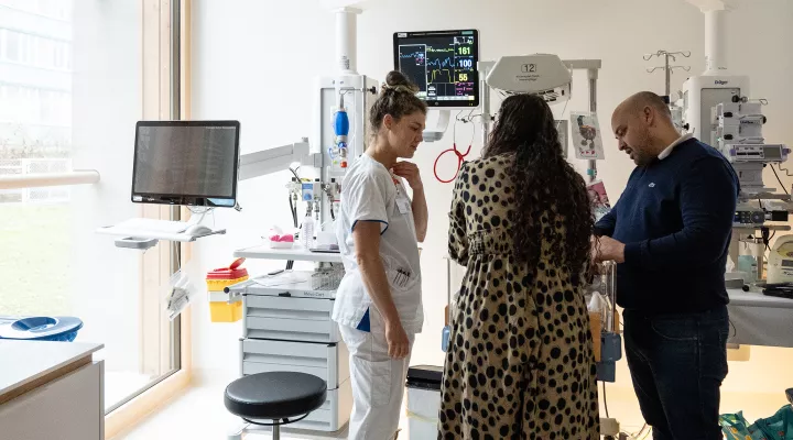 Eine Pflegefachfrau spricht mit einem Elternpaar am Bett eines Neugeborenen auf der Neonatologie