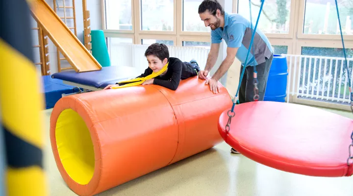 Kinder-Reha Schweiz, Physiotherapie, Therapeut mit Patient im Therapieraum beim Trainingsparcours