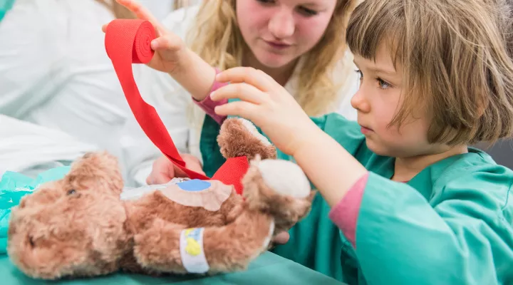 Ein Mädchen macht eine Verbansdwechel bei einen Teddybär