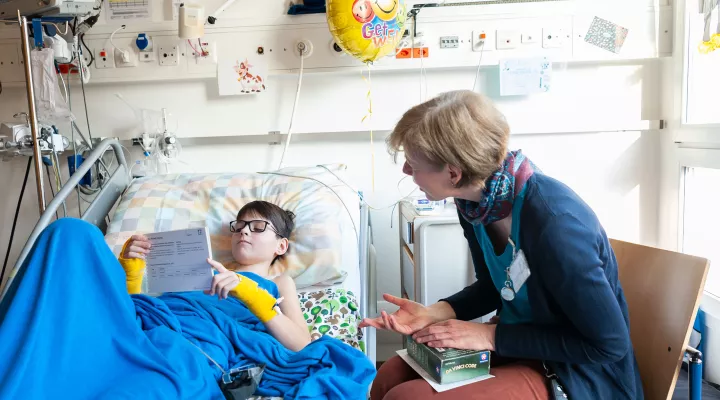 Eine Lehrerin von der Spitalschule gibt einem jungen im Patientenbett Unterricht